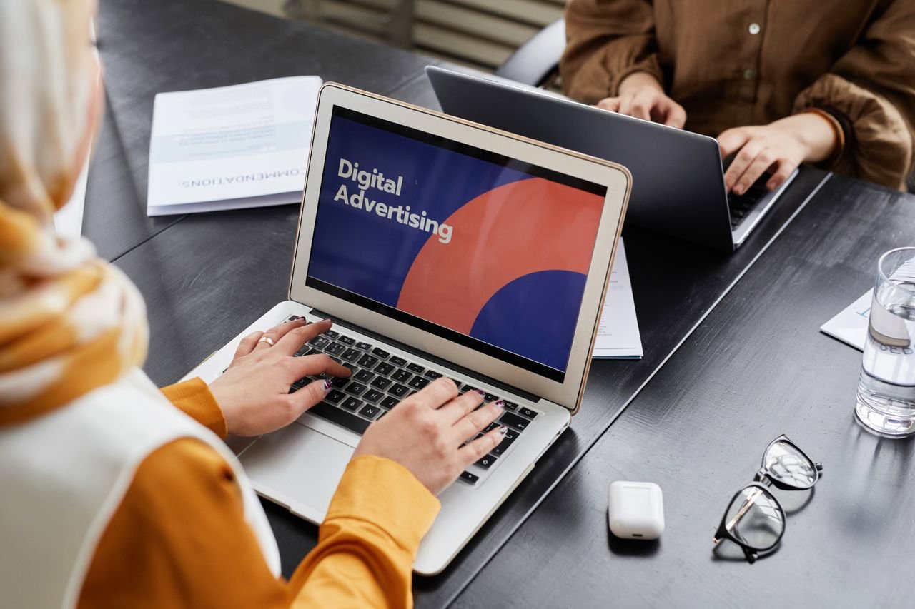 Two professionals work on laptops focusing on digital advertising in an office setting.